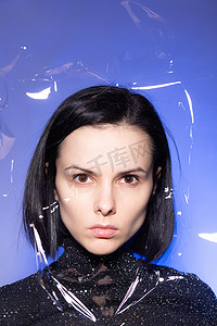 身穿蓝色背景亮片黑色高领毛衣、嘴唇紫色的女人，通过塑料薄膜拍摄照片