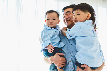 父亲节摄影照片_快乐的父亲带着两个孩子在他们家的卧室里。