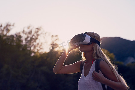 日出时分，一位女士戴着 VR 护目镜徒步旅行，探索虚拟宇宙。