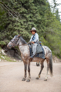 蒙古骑马摄影照片_可爱、微笑的亚洲男孩骑马在山里骑行