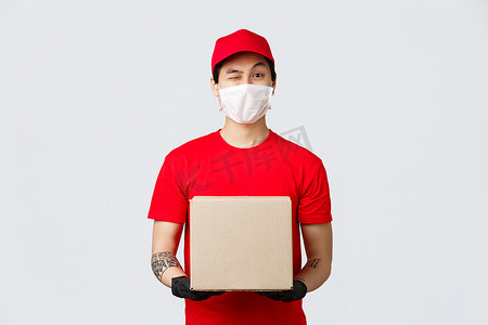 身穿红帽和 T 恤的友好亚洲送货员，佩戴防护手套和医用口罩，以确保客户和员工的安全，在 covid-19 检疫期间送货上门，装箱包裹