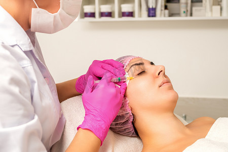 这位年轻的白人女性正在一家美容诊所接受面部注射，在眼睛上注射透明质酸。