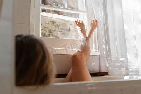 一位美丽的成熟女性在浴缸里用蜡烛按摩双腿，气氛温馨舒适
