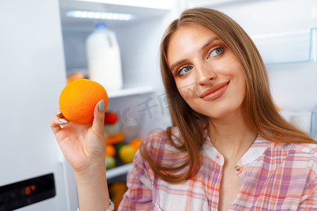一位年轻金发女子从冰箱里拿食物的肖像