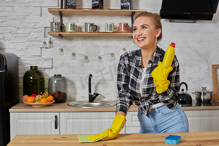 超值服务摄影照片_戴着橡胶手套的年轻妇女或家庭主妇在家庭厨房用超细纤维布擦拭桌子。