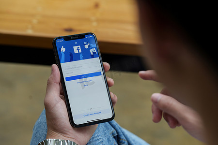 泰国清迈 — 2022年8月25日：一名男子手持苹果iPhone，屏幕上有facebook应用程序。facebook是一款智能手机照片共享应用程序。 