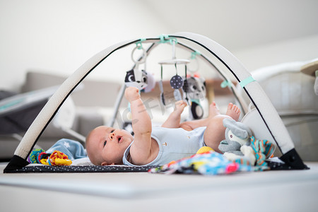 可爱的小男孩在家里的垫子上玩悬挂的玩具拱门 婴儿活动和游戏中心，用于婴儿早期发育。