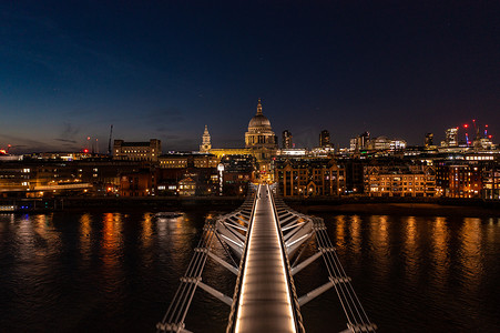 灯光闪烁摄影照片_伦敦市千禧桥走道的鸟瞰图，灯光闪烁，人们在夜间面向教堂圆顶行走