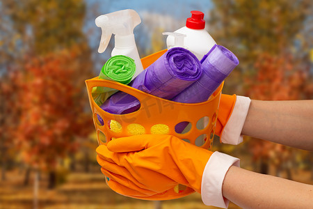 女人的手戴着防护手套，上面有垃圾袋，米色背景的橙色篮子里装着玻璃清洁剂瓶。
