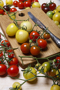 白桌上的小红、黄、绿和黑樱桃番茄，配有木切板、自然背景。