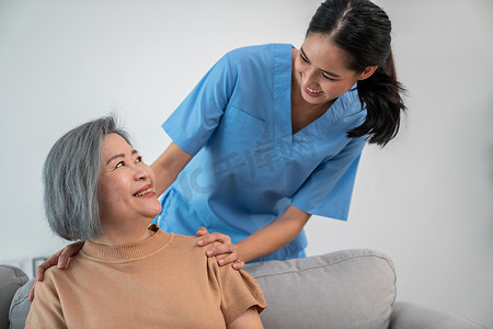 心满意足摄影照片_一名护理人员将双手放在一位心满意足的老年患者的肩膀上。