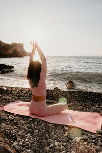 瑜伽摄影照片_中年漂亮的黑发女人在圆石滩附近的海边瑜伽垫上用戒指做普拉提。