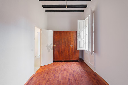 白色房间内部配有木制衣柜、黑色横梁、窗户和镶木地板上的引导标记