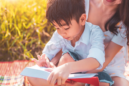 亚洲小男孩和他的母亲在草地上阅读故事书。