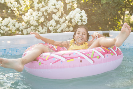 炎热的夏日，快乐的小女孩在室外游泳池里玩彩色充气环。