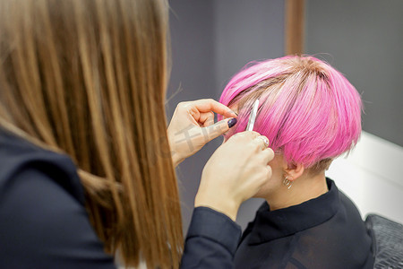 美发师正在为一位年轻女子染上粉红色的短发，准备在美容院进行手术。