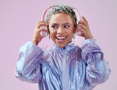 黑人女性在工作室里拿着耳机，用粉红色的墙壁进行音乐流媒体娱乐。