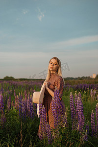 漫步摄影照片_一位戴着草帽的美丽女子走在开满紫色花朵的田野里。