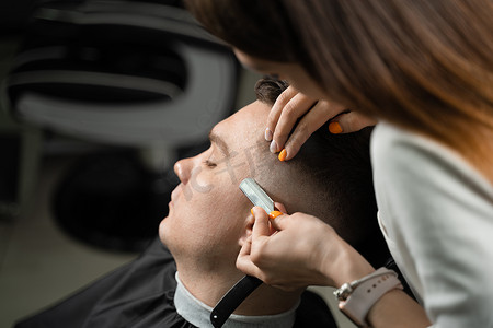 剪头发摄影照片_直剃刀在理发店给男人剪头发。