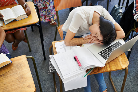 太多的通宵学习……一个学生手臂躺在教室桌子上的高视角。