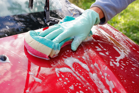 工人在洗车场用海绵洗红色汽车。男手拿着绿色红色海绵洗车。
