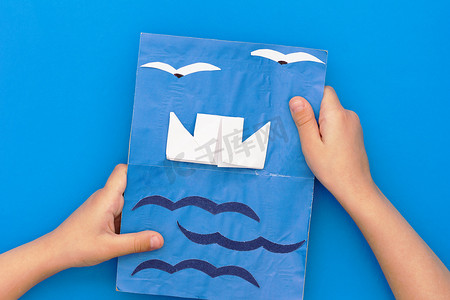 父亲节摄影照片_儿童手中有船海和海鸥的纸艺卡