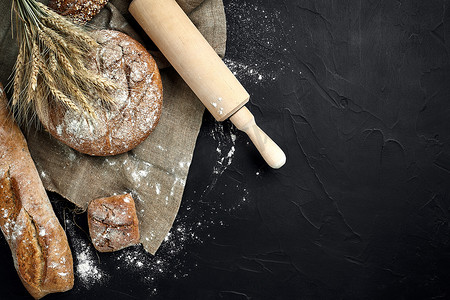 小棍黑板摄影照片_法式长棍面包、烤面包、面粉和小麦穗组合物的顶视图，深色背景上撒有小麦粉