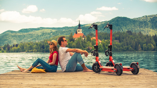 年轻夫妇在度假时探索绿色乡村斯洛文尼亚时，使用电动滑板车作为现代生态交通工具。
