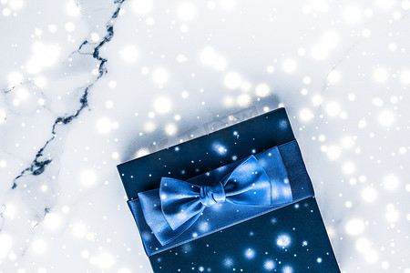 礼盒蝴蝶结摄影照片_冬季节日礼盒，配有蓝色丝绸蝴蝶结、大理石背景上的雪花，作为豪华美容品牌的圣诞和新年礼物，平铺设计