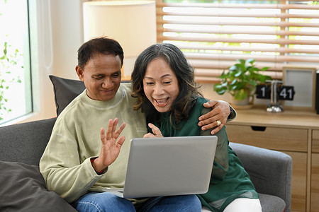 快乐的退休夫妇在家里享受网上冲浪或在笔记本电脑上与家人或朋友进行视频通话的乐趣