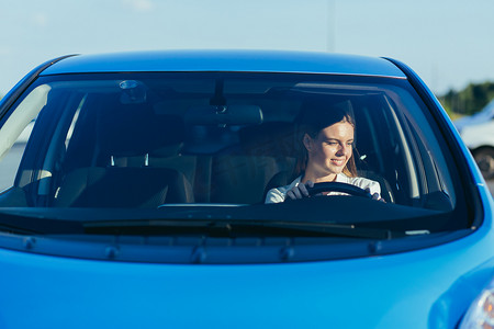 一位成功而幸福的女性驾驶汽车的肖像，从前面透过玻璃拍摄的照片