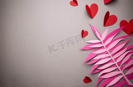 情人节折纸摄影照片_红心是从粉红色背景的纸上剪下来的，纸工艺折纸风格，从上面。
