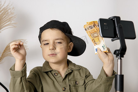 可爱vlog摄影照片_可爱、可爱的小男孩博主记录生活方式博客，拿着钱，在三脚架上与智能手机的相机交谈。