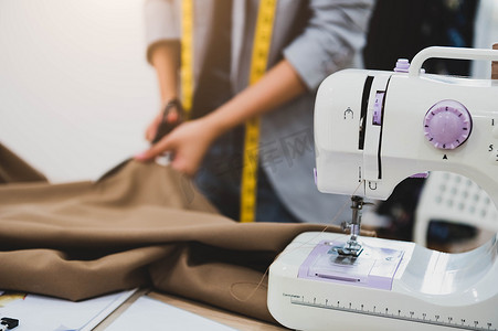 服装面料摄影照片_裁缝师在缝纫机前景的草图线上裁剪服装面料。