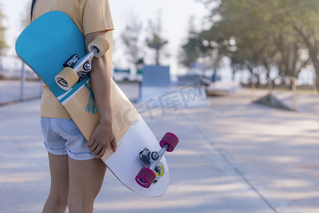 特写年轻女性手持滑板，在公共滑板坡道公园背景上冲浪。