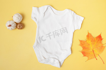 婴儿服装模型顶视图，黄色背景上有南瓜和枫叶，适合秋季的文字或徽标位置