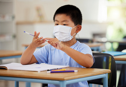 教育、科维德和戴着口罩学习的男孩在课堂上做功课，在小学课桌上写字和数数。
