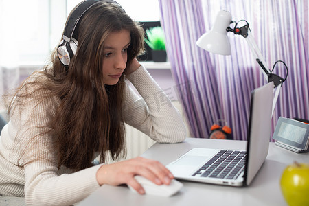 一位年轻的黑发女郎正在通过互联网和笔记本电脑远程在家上学。