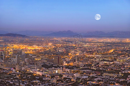在旅游目的地复制城市建筑的空间夜景，包括电灯、基础设施和带有山背景的月亮。