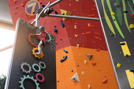 女孩攀岩摄影照片_孩子在游乐中心爬墙。