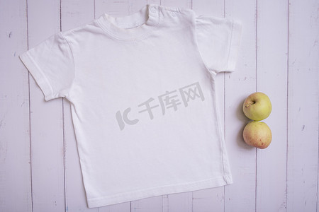 衣服平铺摄影照片_白色儿童 T 恤模型，用于木质背景顶视图上的徽标、文字或设计