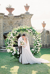 新娘和新郎在古石墙前的婚礼拱门附近拥抱
