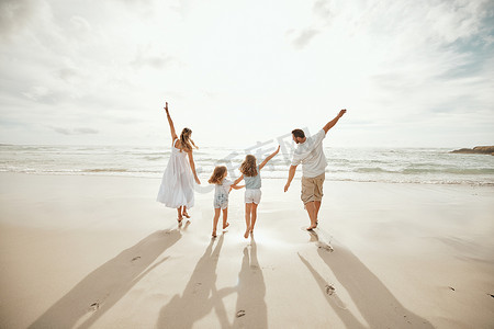 快乐的白人父母带着女儿在海滩上享受空闲时间的背影。