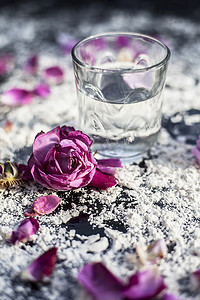 一杯水的特写镜头以及黑板上的一些玫瑰花瓣，上面铺有一些小麦粉。