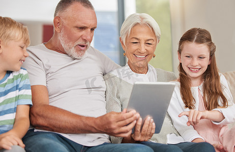 一对幸福的成熟夫妇在家里照顾孩子并使用数字平板电脑时与孙子们建立了亲密的关系。