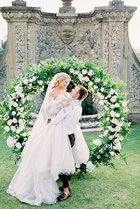 新郎在花园的婚礼拱门上将新娘抱在怀里