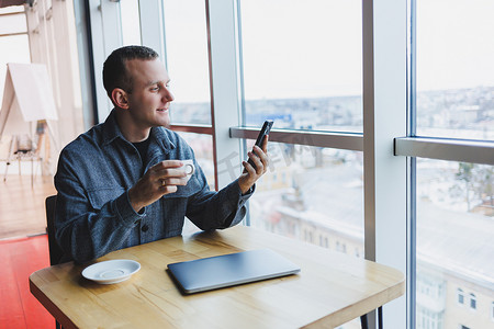 快乐微笑的男经理坐在咖啡馆里使用手机小工具，通过在线应用程序订购送货服务，咖啡馆免费 4g 无线网络，快乐的自由职业者在手机上发短信