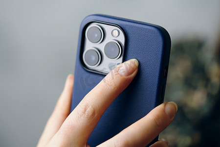 拿苹果手机的手摄影照片_某人拿着装在蓝色保护壳中的 iPhone 13 Pro。