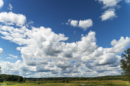 蓝天的背景，有云彩、绿色的田野、河流和森林