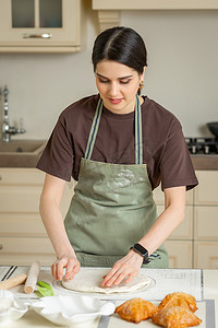 一位身穿绿色围裙的年轻家庭主妇在明亮的厨房里准备自制蛋糕